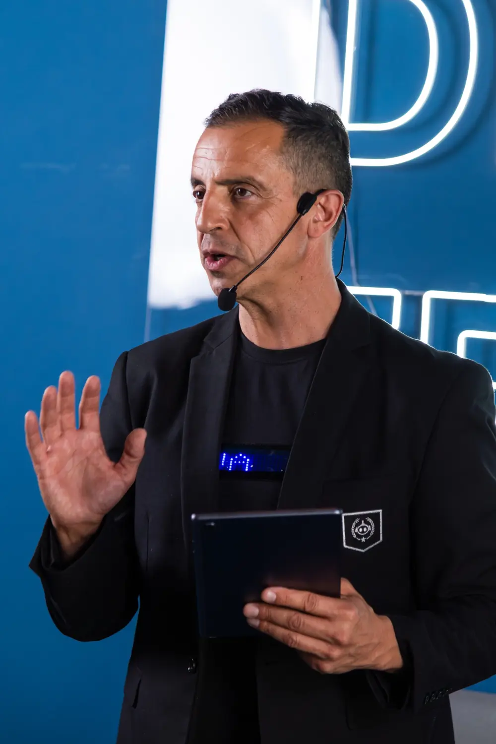 Roberto Menéndez hablando en el escenario con un micrófono, señalando hacia delante.